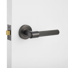 Gunmetal knurled door handle on a white door with a light gray background