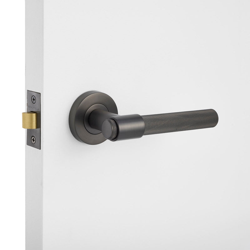 Gunmetal knurled door handle on a white door with a light gray background