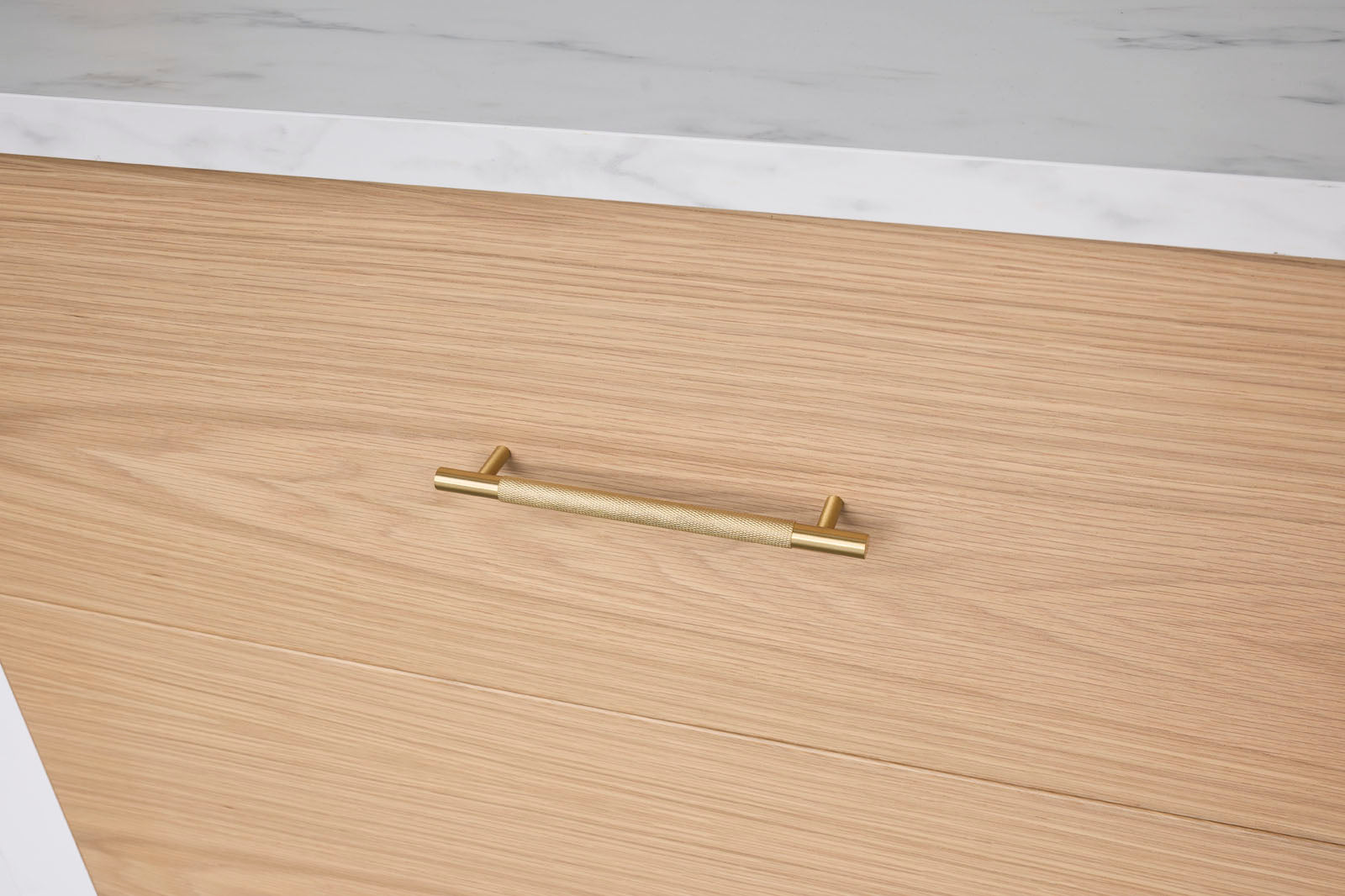Gold handle on a wooden drawer with a white marble countertop in the background