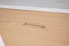 Gold handle on a wooden drawer with a white marble countertop in the background
