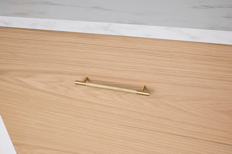 Gold handle on a wooden drawer with a white marble countertop in the background